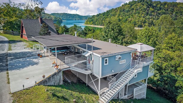 A multi-story building with a balcony and a covered outdoor area, overlooking a lake and forested hills. - The Lazy Lake House on Center Hill (Sparta)