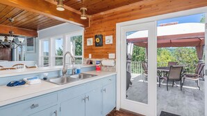 A modern kitchen with a large window, a sink, and a dining area with outdoor seating. - The Lazy Lake House on Center Hill (Sparta)