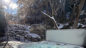 Un jacuzzi en un entorno exterior con un muro de piedra y árboles al fondo.