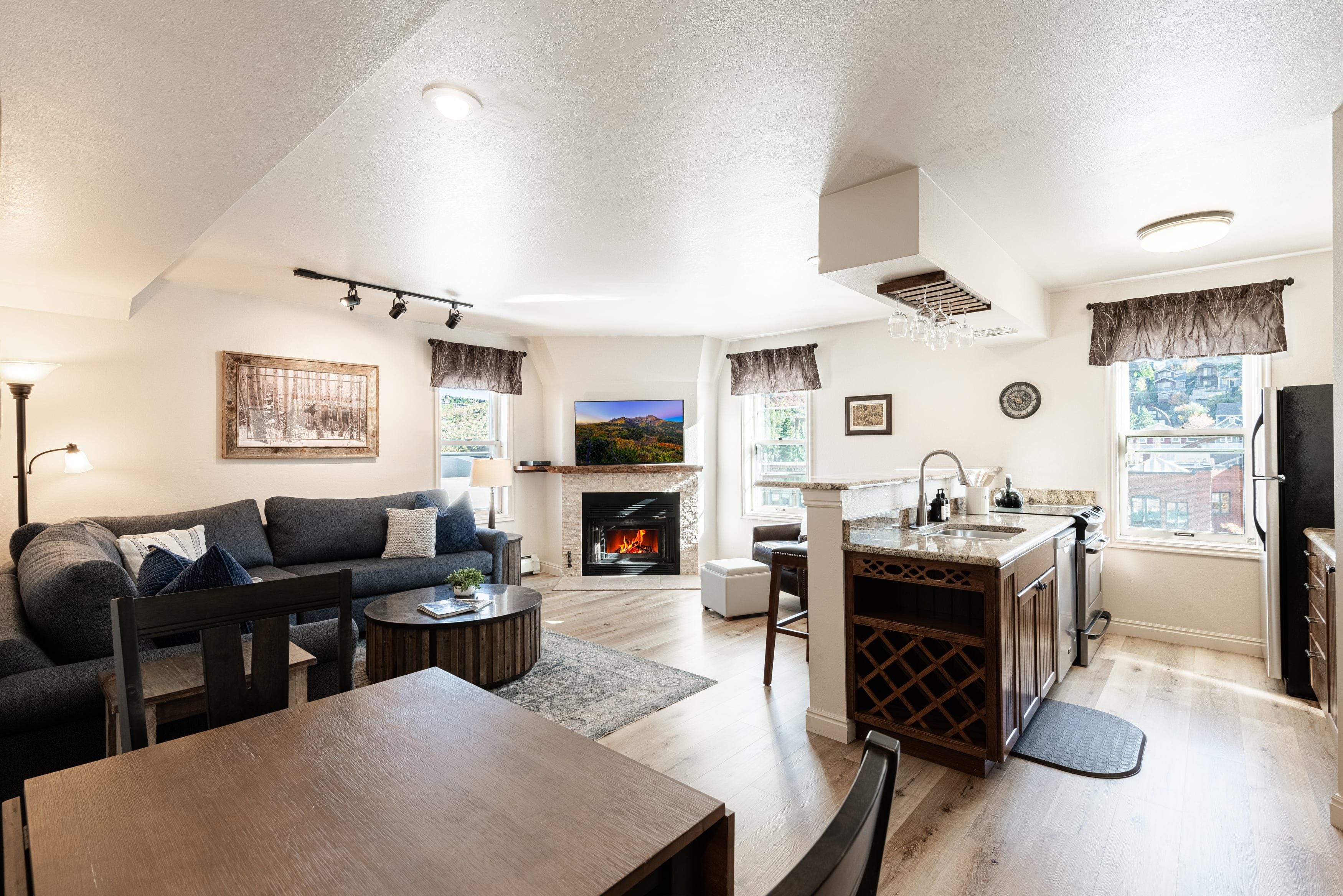 A modern living room with a fireplace, a dining area, and a kitchen with a built-in island.