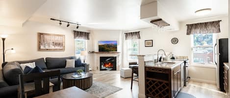 A modern living room with a fireplace, a dining area, and a kitchen with a built-in island.