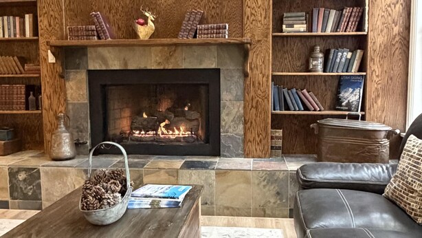 Una sala de estar acogedora con chimenea, estanterías, un sofá de cuero y una mesa de centro.