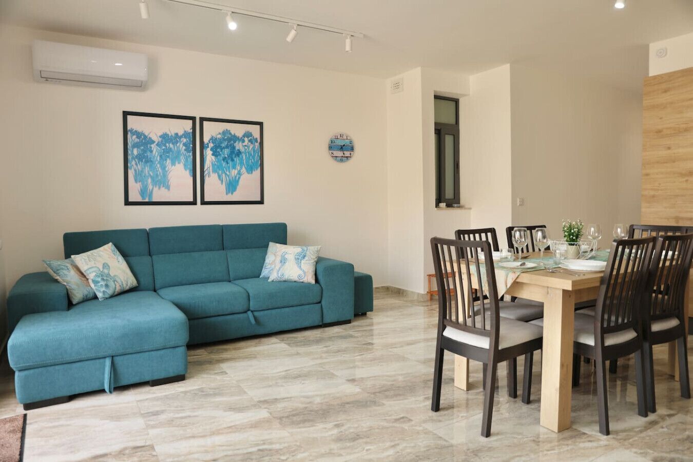 Un salon avec un canapé de couleur turquoise, une table à manger avec des chaises et une horloge au mur.