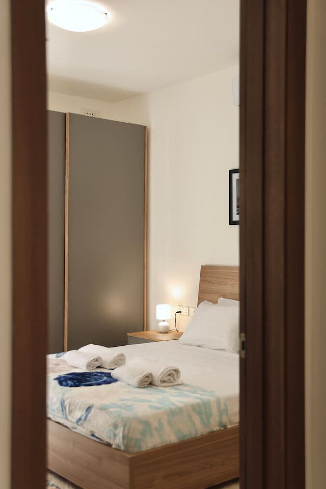 A hotel room with a bed, a nightstand, a lamp, and a wardrobe.