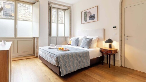 A bedroom with a bed, bedside table, lamp, and a window with a view of trees. - Central & Cozy Studio by HostWise (Vila Nova de Gaia)