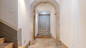 A hallway with a stone floor, a wooden staircase on the left, and a white door at the end. - Central & Cozy Studio by HostWise (Vila Nova de Gaia)