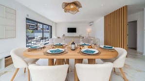 A modern dining room with a wooden table set for six, white chairs, and a hanging light fixture. - Elegant Retreat with Pool & Terrace by HostWise (Alvor)