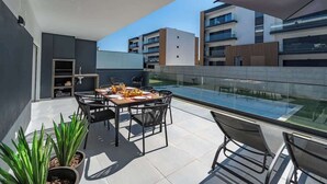 A modern outdoor dining area with a glass table and chairs, surrounded by potted plants. - Elegant Retreat with Pool & Terrace by HostWise (Alvor)