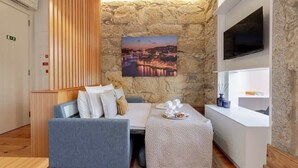 A modern room with a stone wall, a flat-screen TV, a sofa, a small table with a tray, and a painting of a cityscape. - Cozy Studio with Workspace by HostWise (Porto)