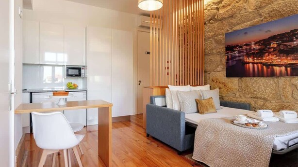 A modern hotel room with a kitchenette, a dining area, and a bed with a cityscape view. - Cozy Studio with Workspace by HostWise (Porto)