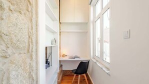 A narrow room with a desk, chair, and shelves against a textured wall. - Cozy Studio with Workspace by HostWise (Porto)