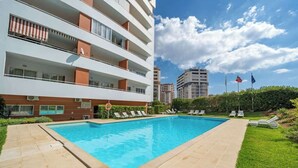 A modern apartment building with a swimming pool, lounge chairs, and a well-maintained garden.