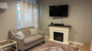 A living room with a beige sofa, a patterned rug, a fireplace, and a flat-screen TV. - Charming Studio in Delightful Richland (Richland)
