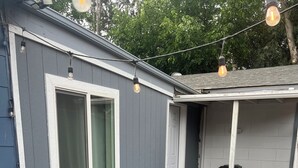 A residential building with a grey exterior, a white door, and a window with a green curtain. There are stepping stones on a gravel path leading to the door. - Charming Studio in Delightful Richland (Richland)