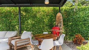 Eine Außenpatio mit einem runden Holztisch, weißen Stühlen und einem roten Grill.