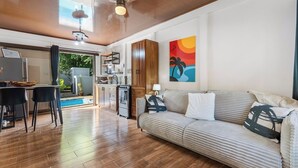 Ein modernes Wohnzimmer mit einer Couch, einem Essbereich mit Stühlen, einer Küche mit Holzausbau und einem Pool, der durch die Glastür sichtbar ist.
