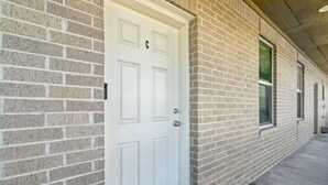 A white door with a number 'C' above it, set in a brick building with windows and a concrete floor. - Sunny Hidden Retreat C – Ocean Town Gem (Galveston)