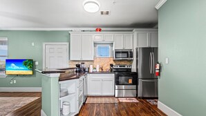 A kitchen with white cabinets, stainless steel appliances, and a wooden floor. - Sunny Hidden Retreat C – Ocean Town Gem (Galveston)