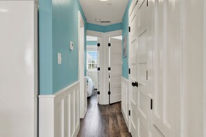 A hallway with white doors and teal walls, leading to a room with a bed and a window.