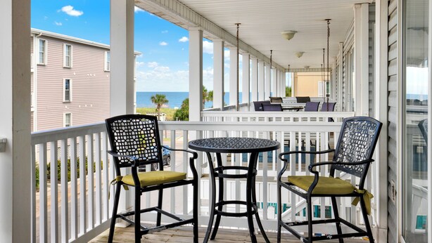 Un balcone riparato con due sedie e un tavolino, vista su una zona residenziale e l'oceano.
