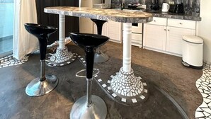 Una cocina moderna con gabinetes blancos, encimera de mármol y taburetes negros.