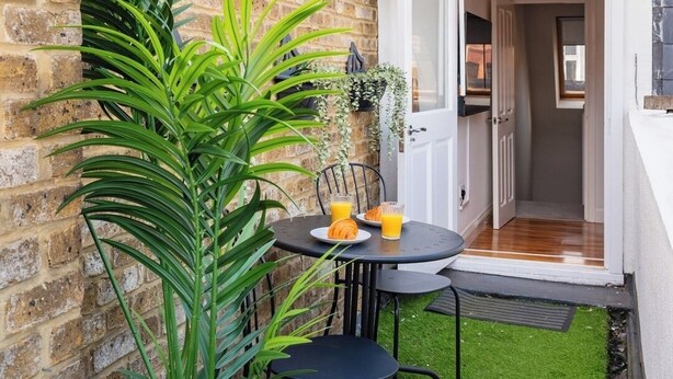 A small patio area with a brick wall, a green lawn, and a table with chairs.
