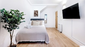 A modern bedroom with a bed, a large mirror, a wall-mounted TV, and a potted plant.