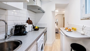 A compact kitchen with a built-in oven, a coffee maker, and a toaster. There is a small sink and a window above the sink.