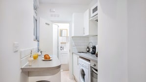 A compact kitchen with a washing machine, a sink, and a small dining area with a chair.