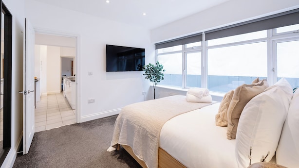 Un dormitorio moderno con una cama grande, un televisor de pantalla plana montado en la pared y una ventana con vistas.