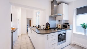 Una cocina moderna con armarios blancos, una isla central, electrodomésticos de acero inoxidable y un ventanal amplio.