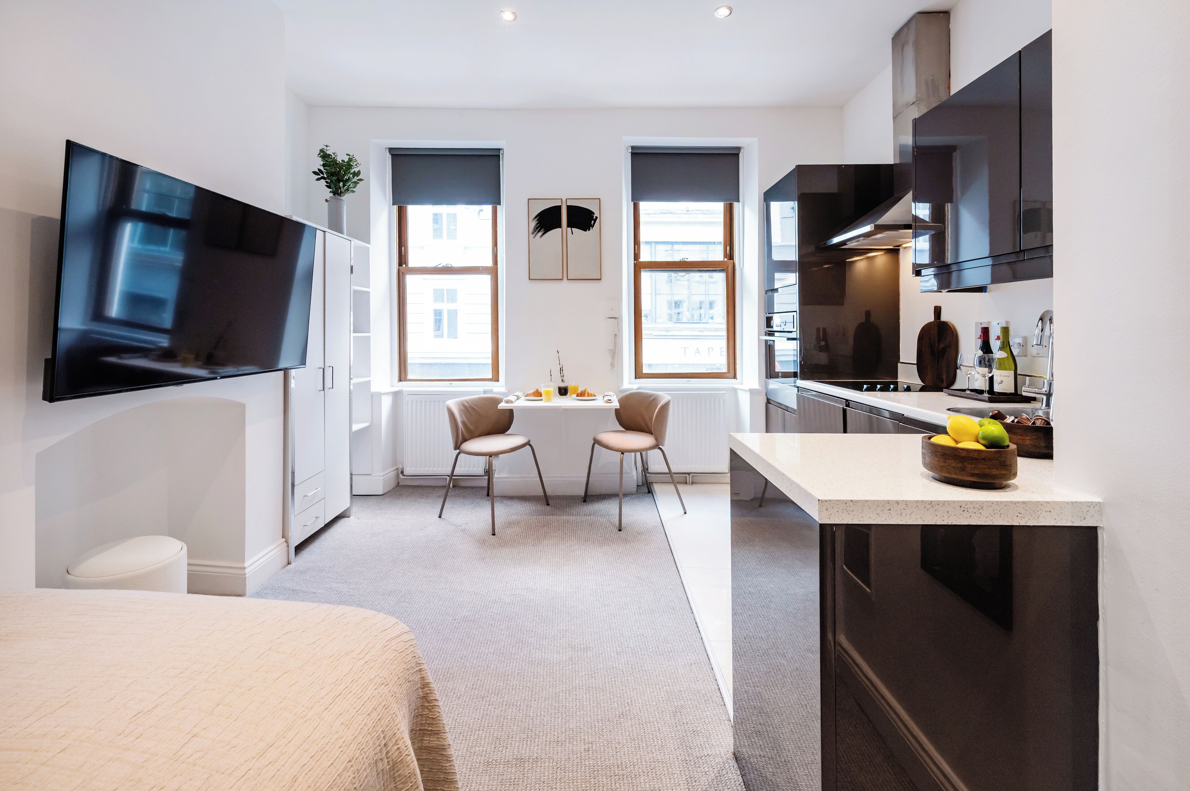 A modern kitchen with dark cabinets, a large TV, and a dining area with two chairs and a table. - Soho Studio w/ Kitchen, 1BD/1BA (Greater London)