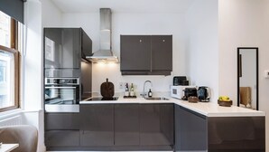 A modern kitchen with dark cabinetry, stainless steel appliances, and a central island. - Soho Studio w/ Kitchen, 1BD/1BA (Greater London)