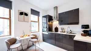 A modern kitchen with a dining area, featuring a large window, dark cabinets, and a built-in oven. - Soho Studio w/ Kitchen, 1BD/1BA (Greater London)