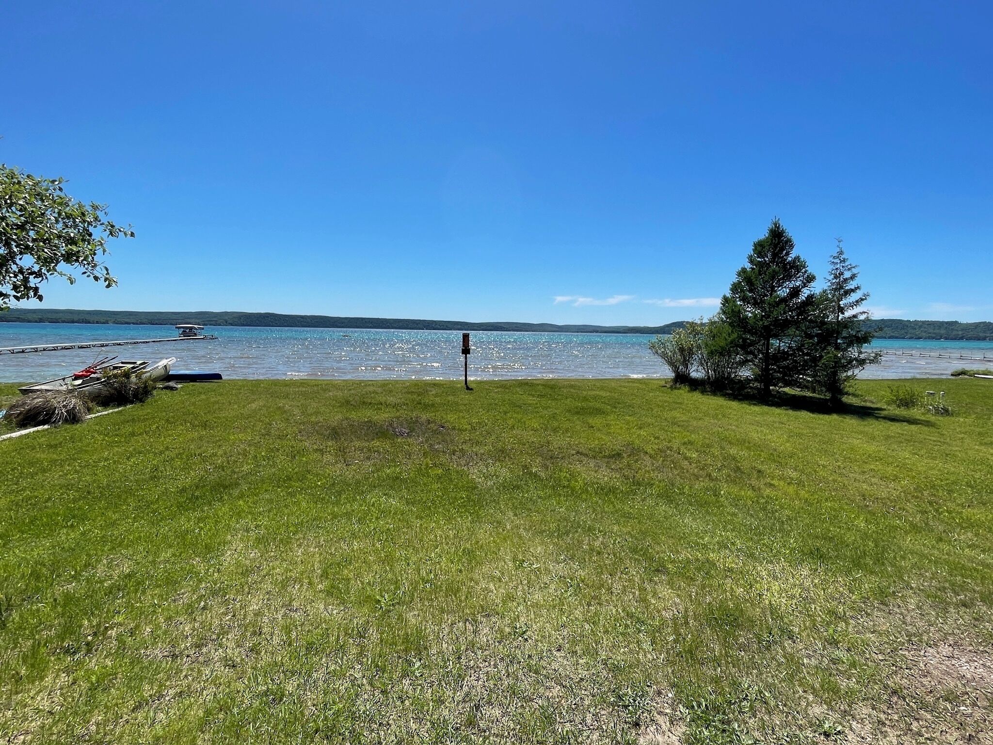 A grassy area with a body of water, a dock with boats, and a clear sky.