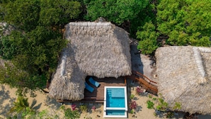 An aerial view of a resort with thatched-roof huts, a swimming pool, and lush greenery.