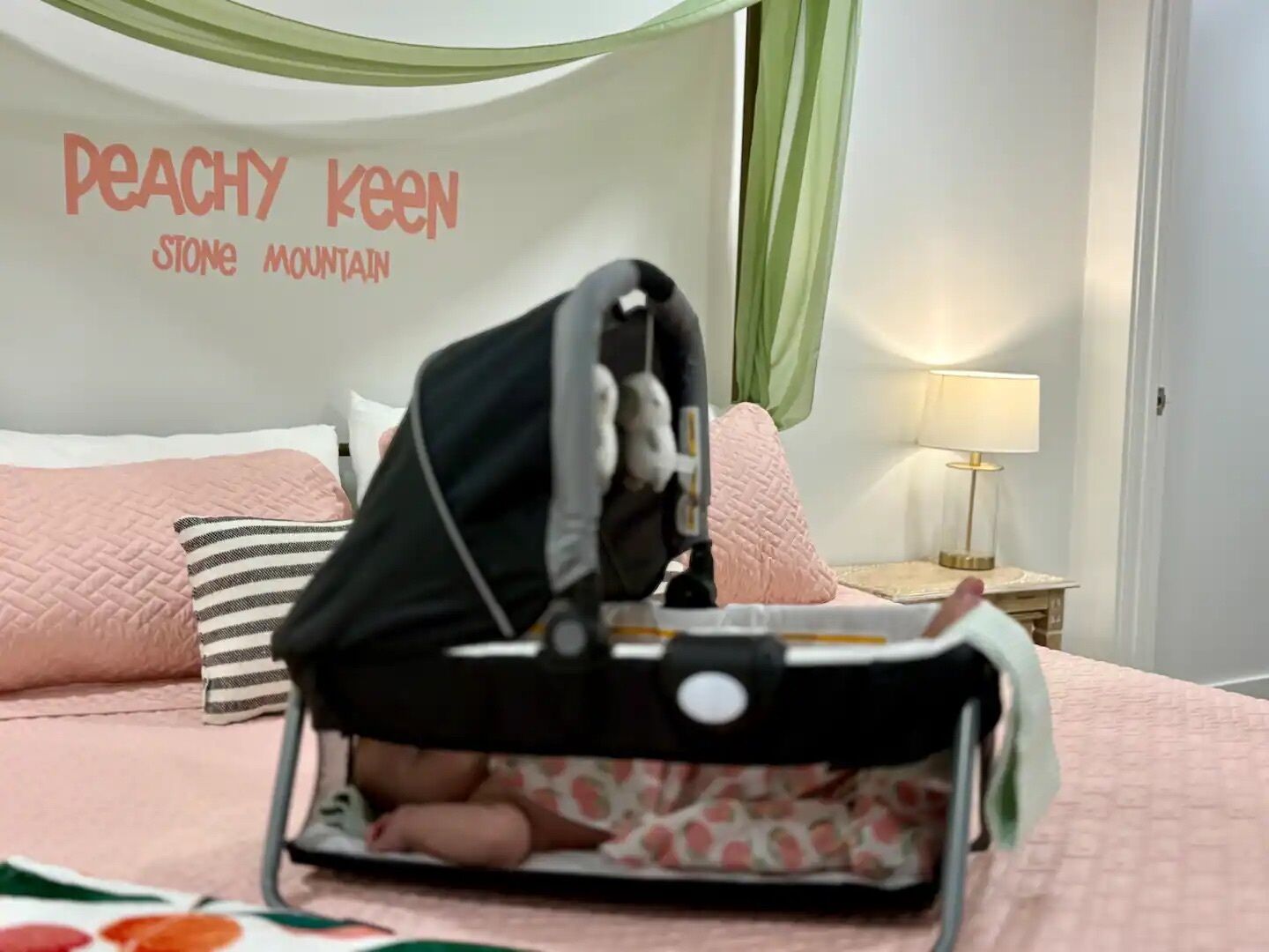 A bed with a pink quilt, a striped pillow, and a wall with the text "Peachy Keen Stone Mountain".