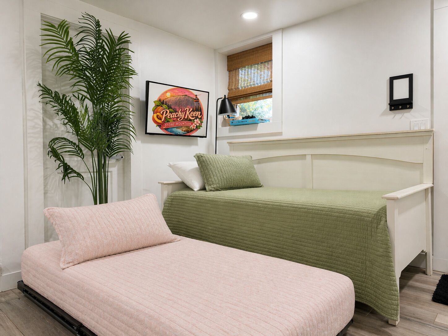 A bedroom with a bed, a plant, a framed picture, and a window with blinds.