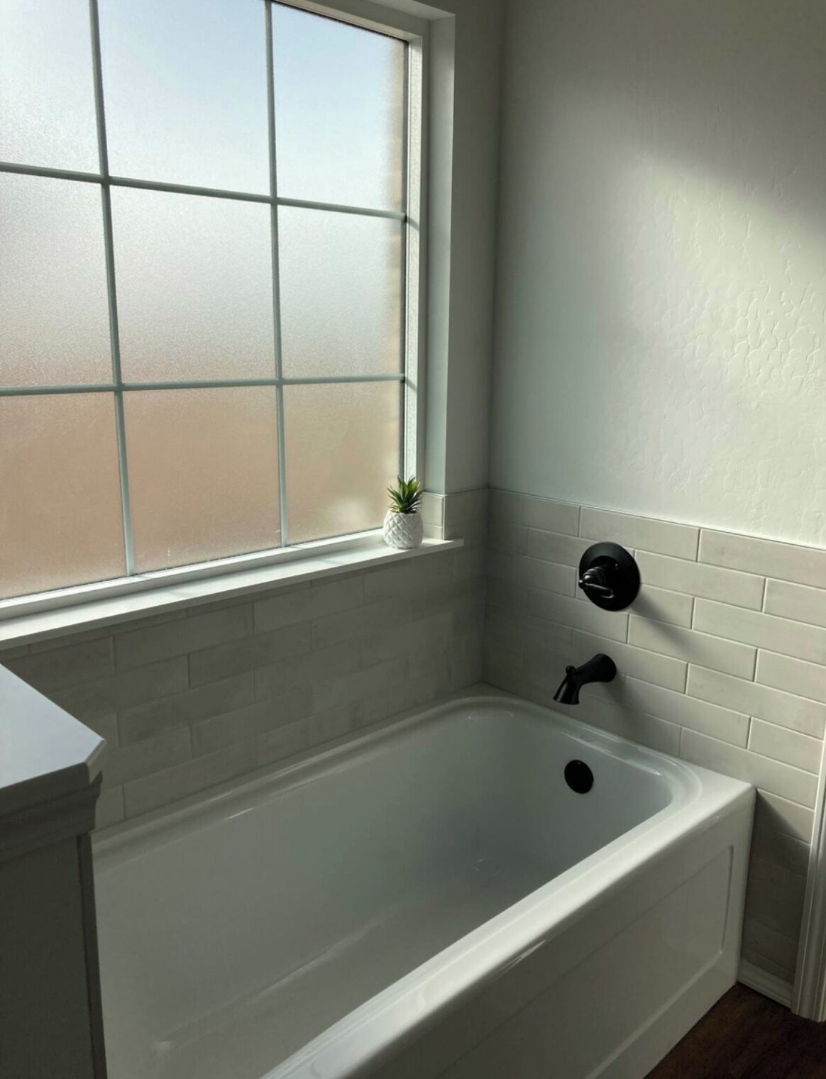 A bathroom with a white bathtub, a window with frosted glass, and a small potted plant on the windowsill.