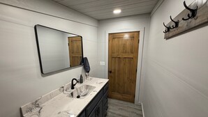 A bathroom with a marble sink, dark cabinets, a wooden door, and a mirror. - Boar's Tusk Lodge (Winner)