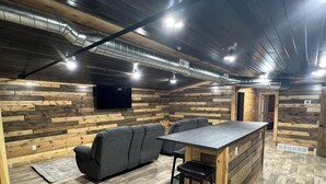 A cozy room with a wooden wall, a sofa, a small bar area, and a TV mounted on the wall. - Boar's Tusk Lodge (Winner)