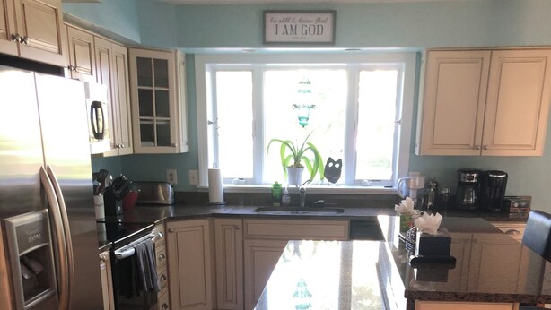 Una cocina con armarios de madera, un refrigerador de acero inoxidable, un fregadero y una ventana con vistas a zonas verdes.