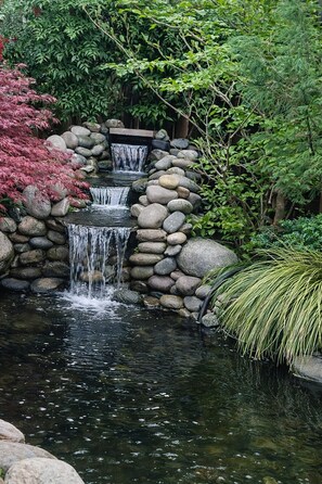 A multi-tiered waterfall in a garden with rocks and foliage.