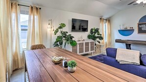 A modern living room with a wooden dining table, a blue sofa, and large green plants.