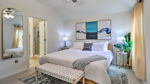 A modern bedroom with a large bed, bedside tables, a bench, a ceiling fan, and artwork on the wall.