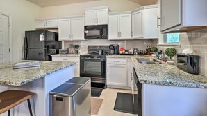 A modern kitchen with white cabinets, granite countertops, stainless steel appliances, and a small island with stools.