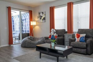 A modern living room with a sofa, armchair, coffee table, and a sliding glass door leading to an outdoor area.