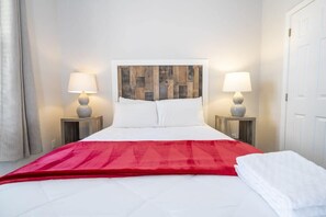 Une chambre d’hôtel avec un lit, deux lampes de chevet, un plaid rouge et une porte blanche.