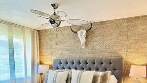A modern bedroom with a tufted headboard, a large bed with white bedding, a side table with a lamp, and a wall-mounted skull decoration. - Urban Cowboy Condo – Scottsdale, AZ (Scottsdale)