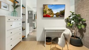 A modern room with a white dresser, a desk, a large TV on the wall, and a potted plant. - Urban Cowboy Condo – Scottsdale, AZ (Scottsdale)